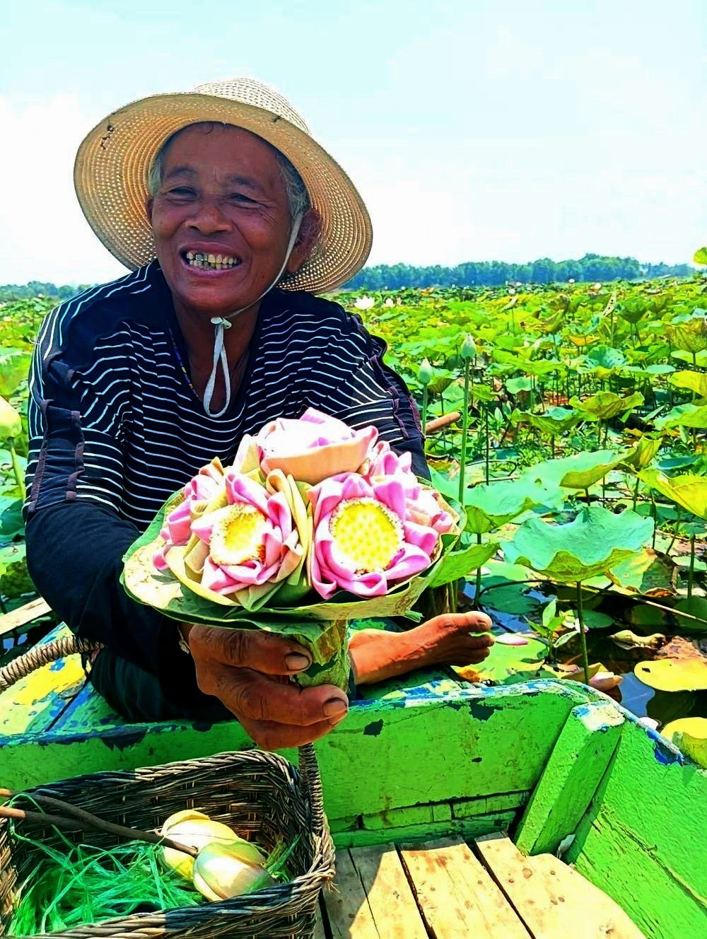 A smiling Cambodian lotus seller holding pink lotus flowers