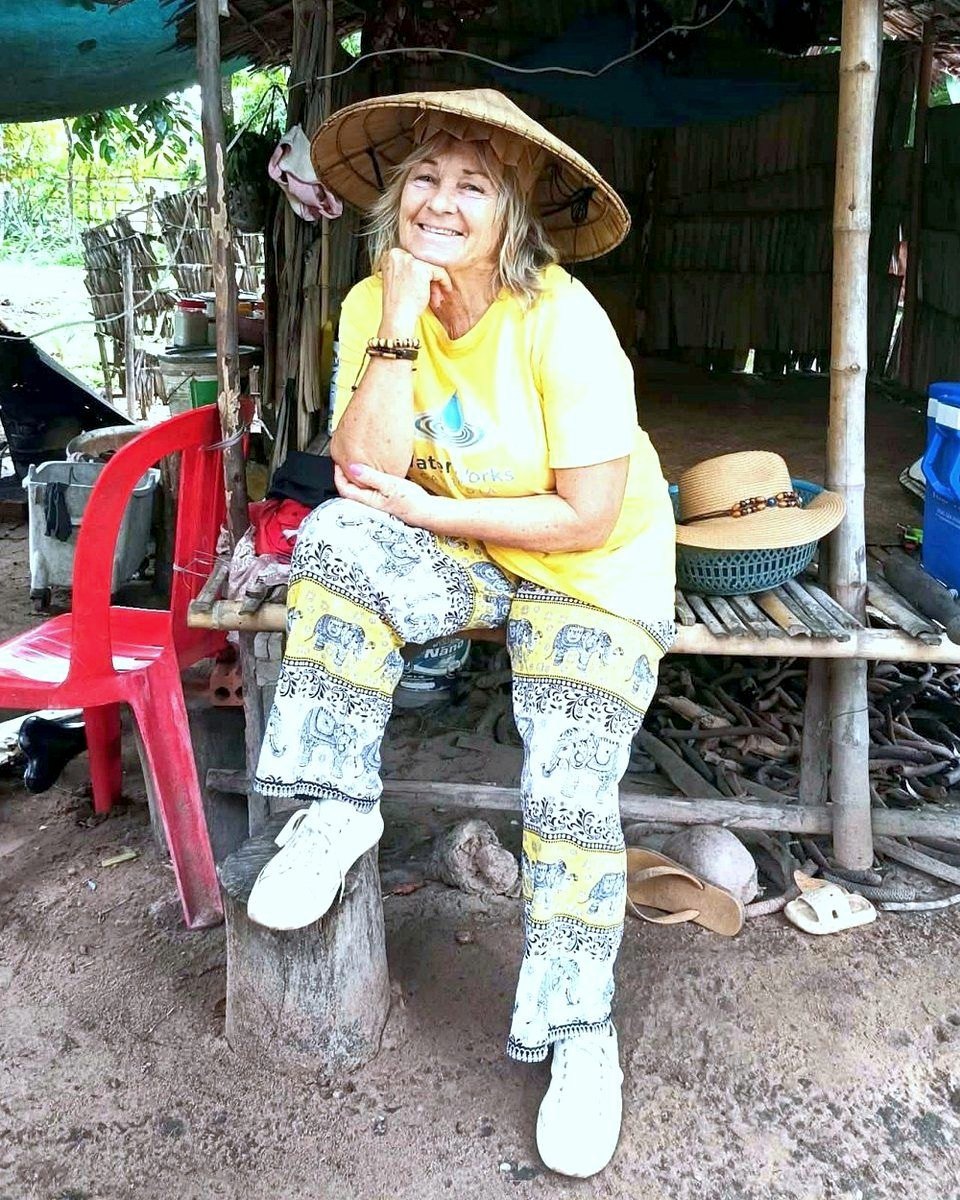 Deb Daniels in a conical hat outside a village home